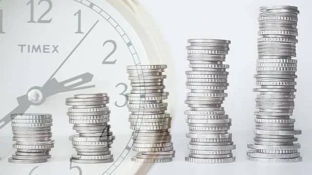 stack of coins in front of a clock