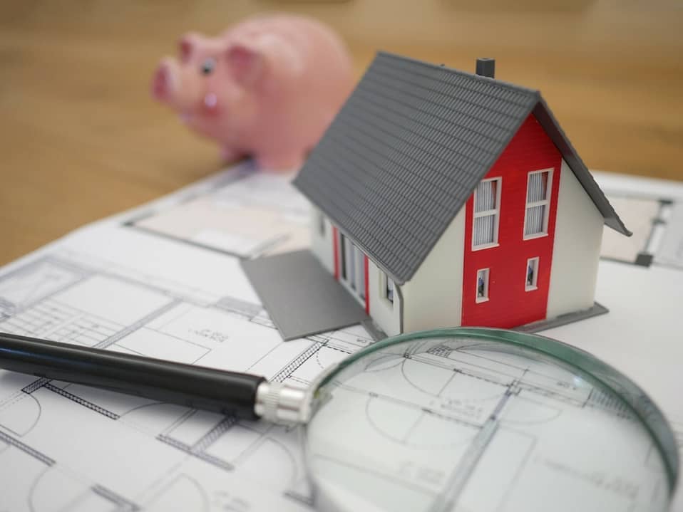 house on top of a blueprint with a piggy bank in the background